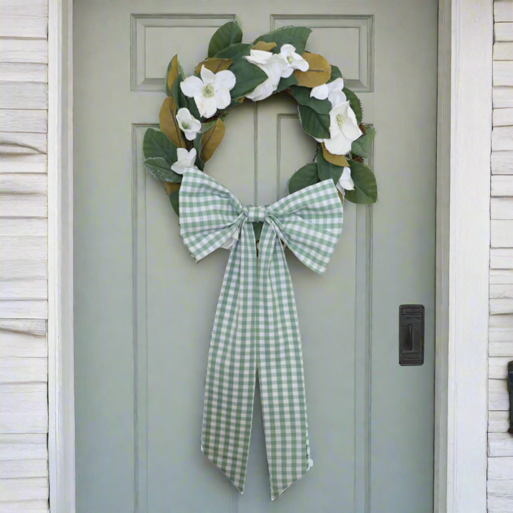 Decorative wreath with green leaves and white flowers, tied with a green and white checkered ribbon on a white background.