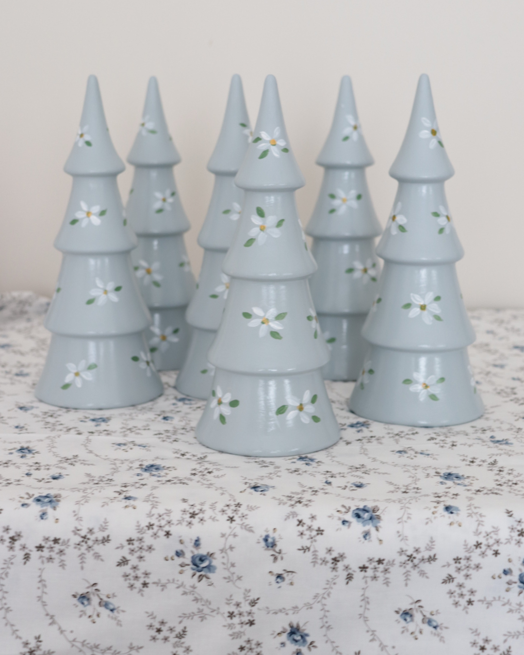 Set of light blue ceramic Christmas trees with floral patterns on a floral tablecloth.