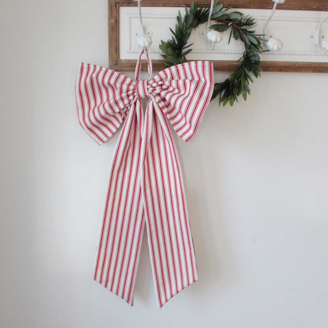 Red and white striped bow hanging on a wall with a wreath in the background.