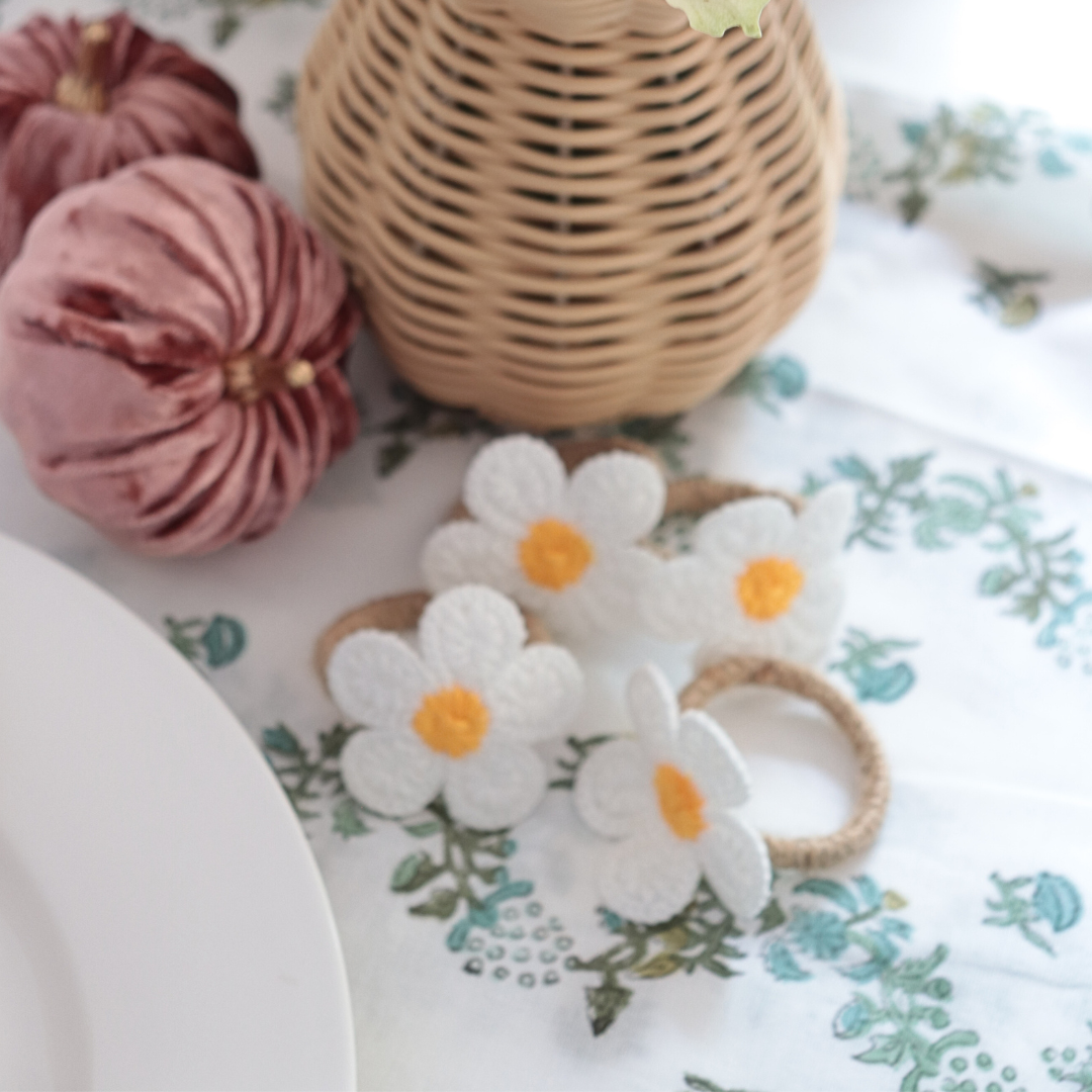 Two floral-patterned hair ties on a decorative tablecloth with a woven basket and pink fabric in the background.