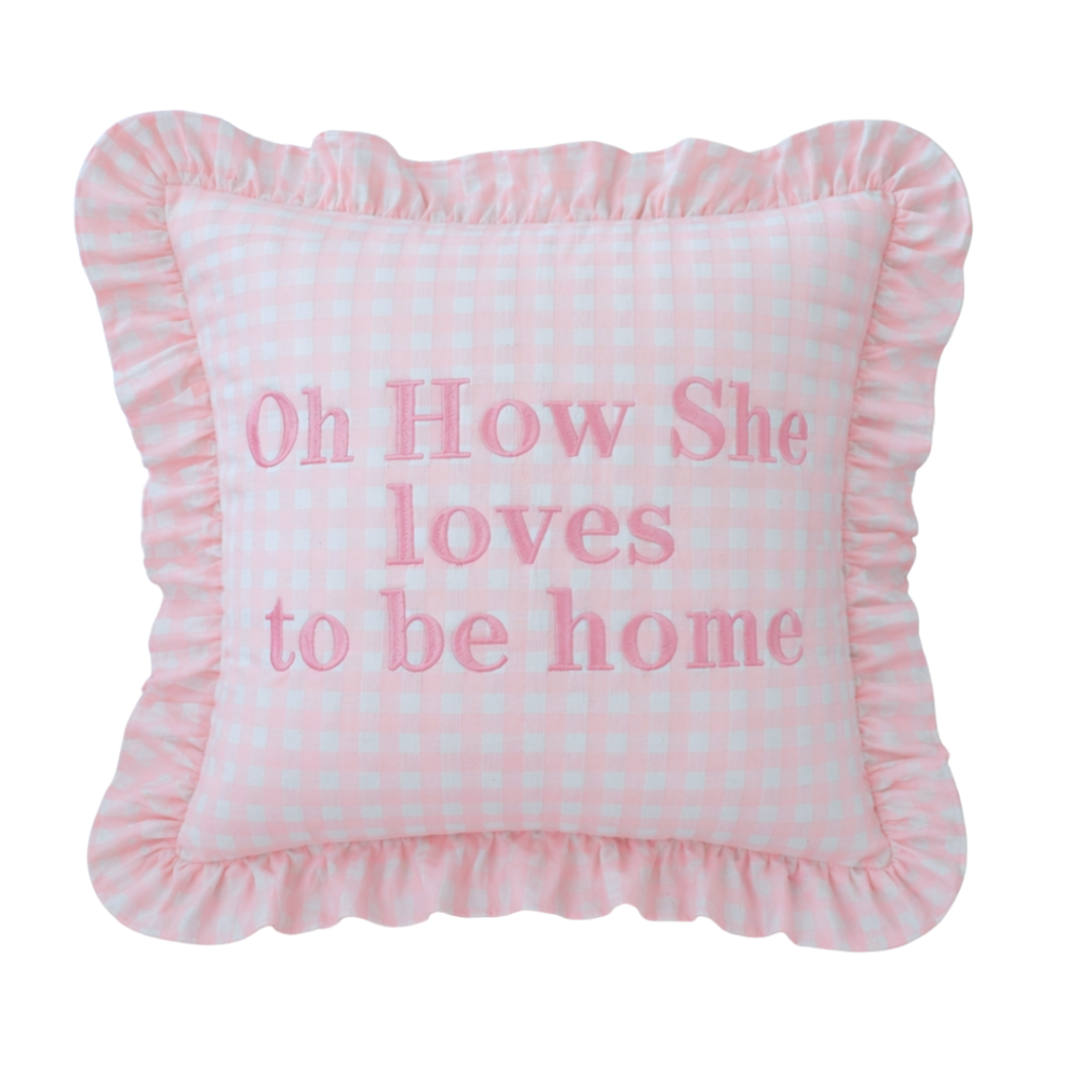 Pink pillow with text 'Oh How She loves to be home' on a white background