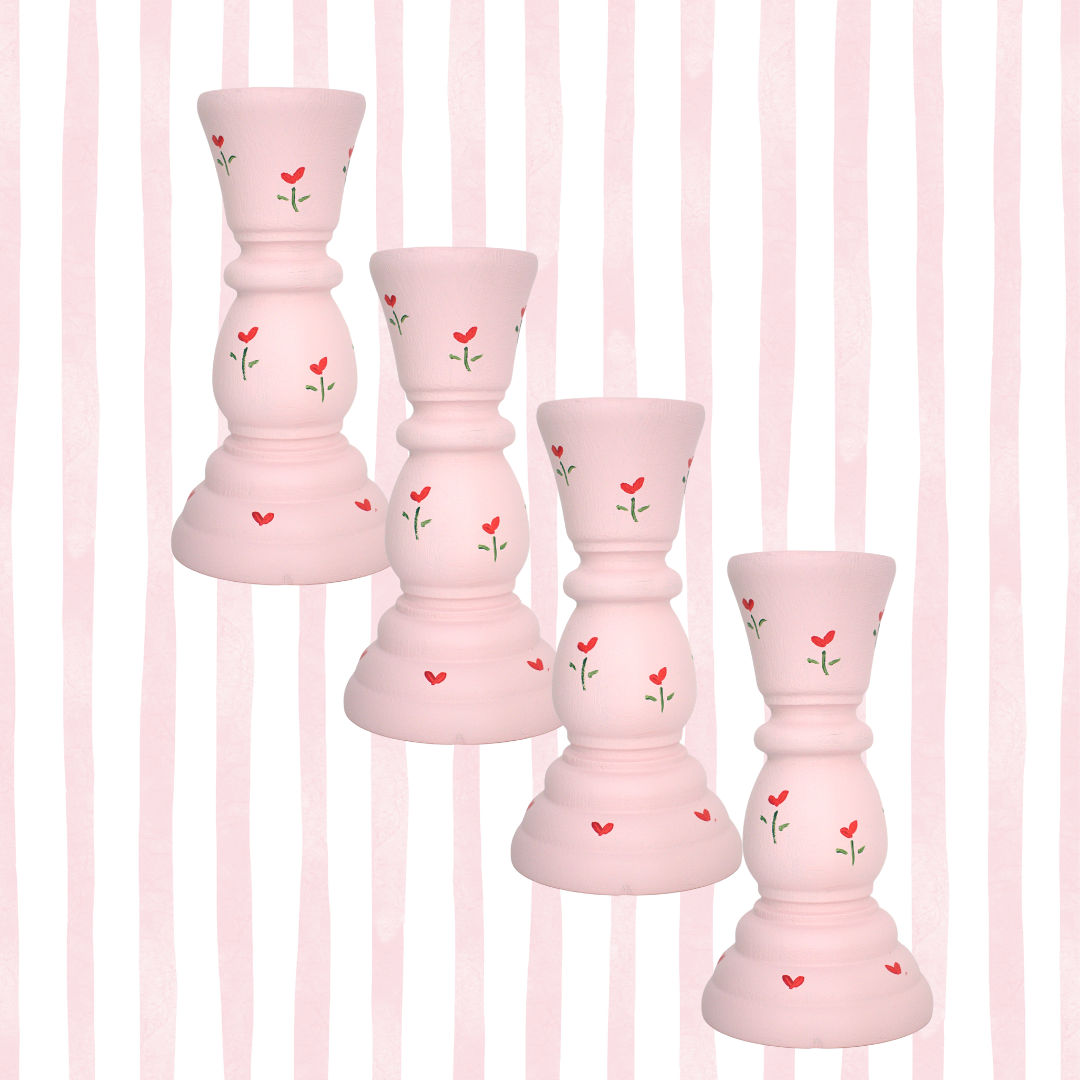 Set of pink candle holders with red heart and green stem designs on a pink striped background