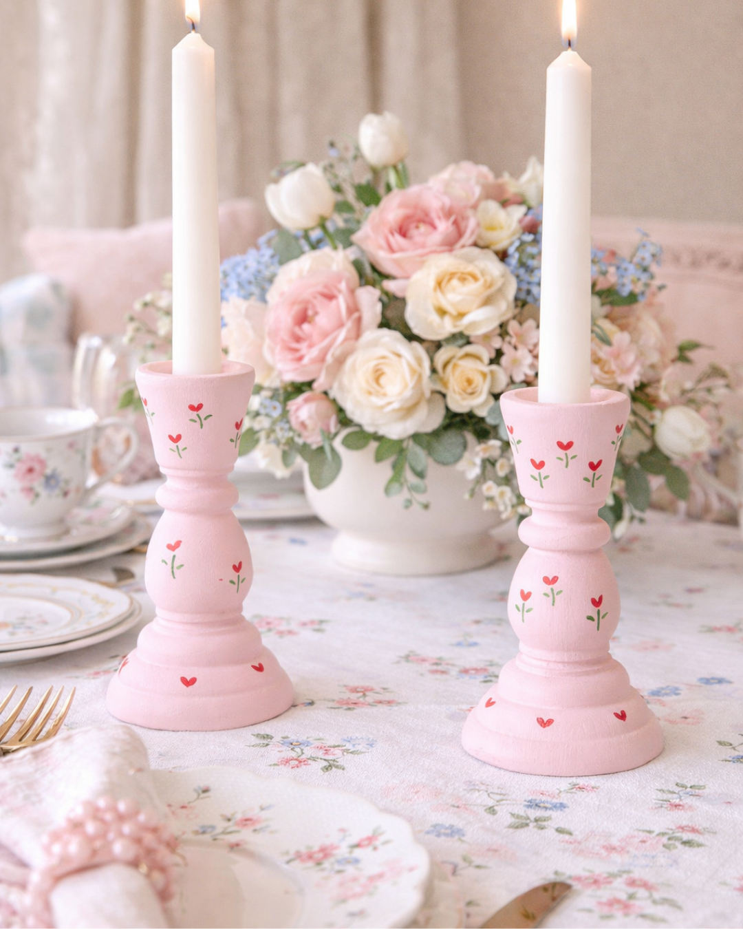 Pink candle holders with heart designs on a table with flowers and tea cups.
