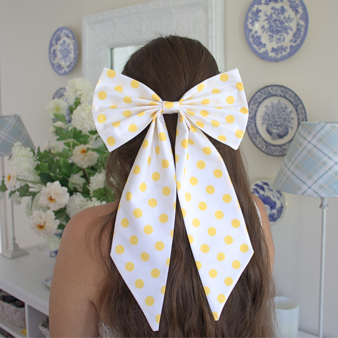 Person with a large white polka dot bow in their hair, set against a decorative room background.