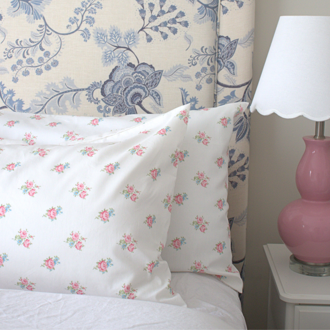 Floral-patterned pillows on a bed with a decorative headboard and pink lamp.