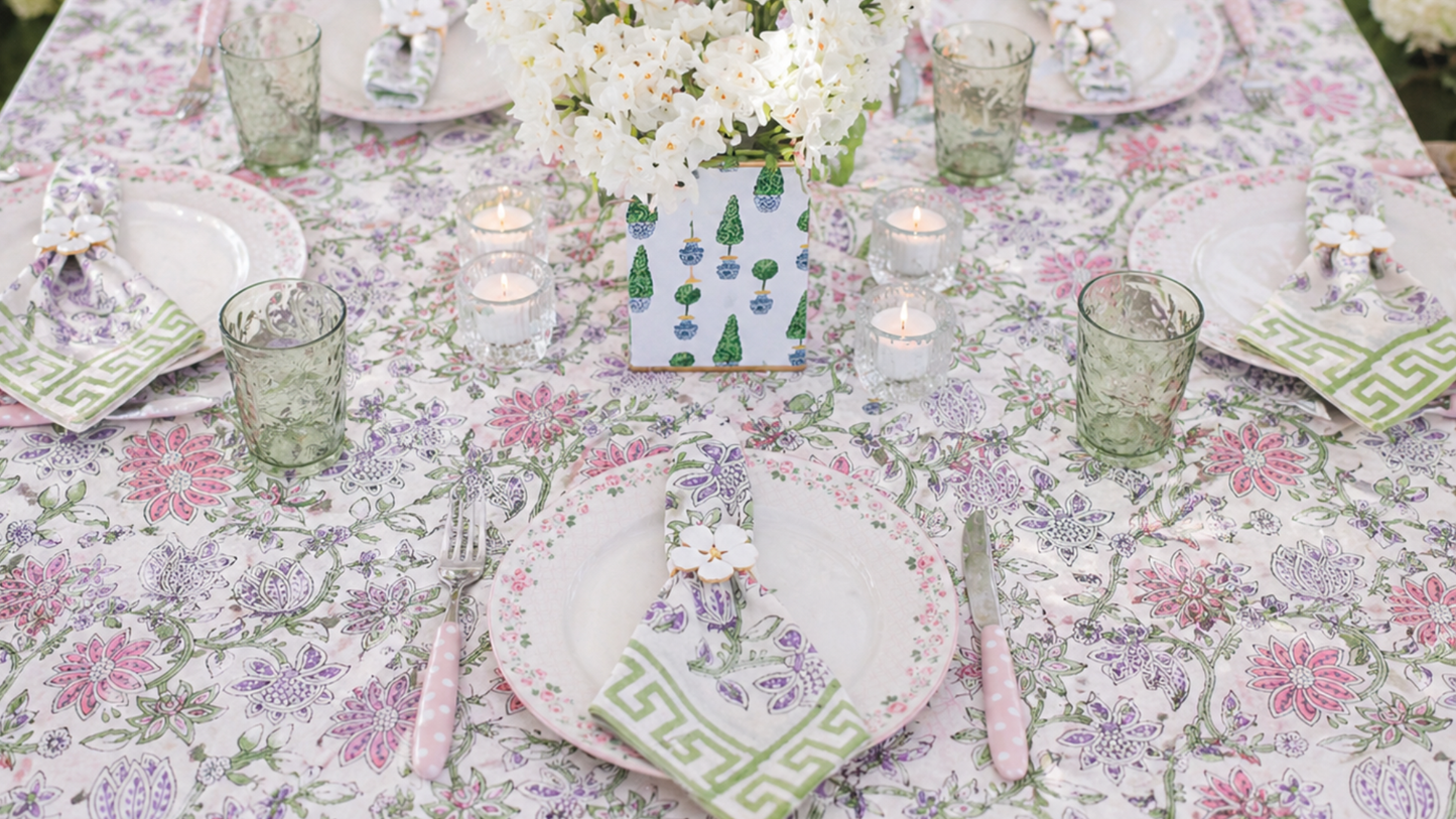 Elegant table setting with floral tablecloth, plates, glasses, and candles.