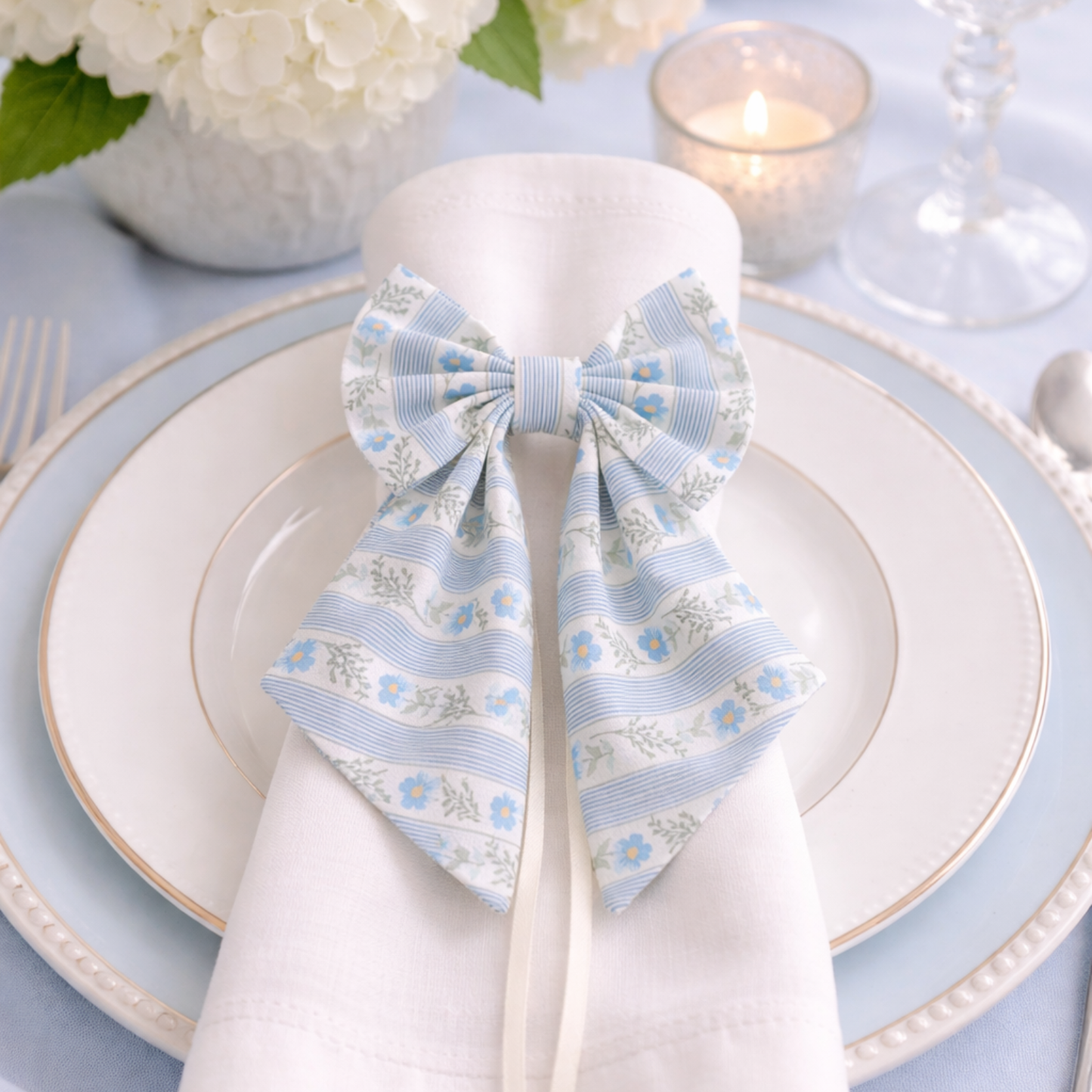 Napkin with a decorative bow on a table setting with plates and candles.