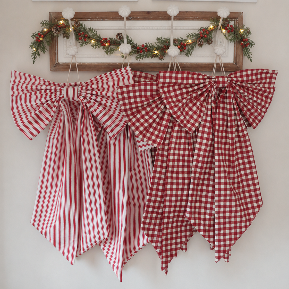Two large fabric bows in holiday patterns hang on a white wall. One bow has red and white vertical stripes, and the other has a red and white gingham check.