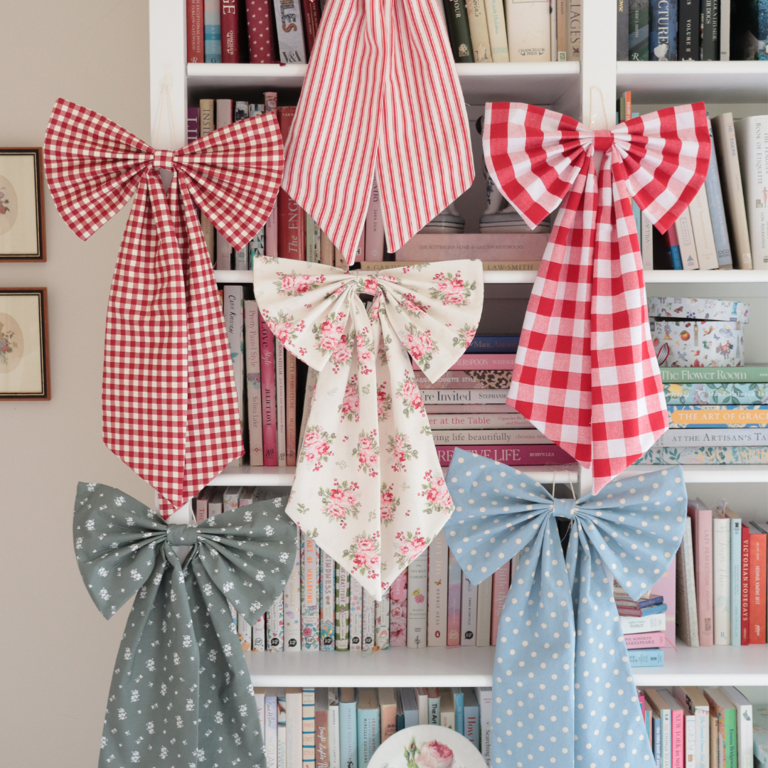 Six fabric bows in various patterns (gingham, stripes, floral, polka dot) hanging on a white bookshelf.
